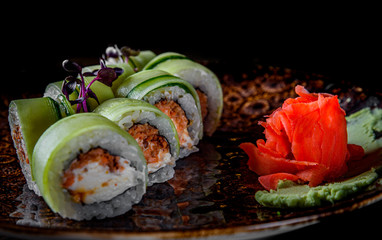 sushi roll with tuna, cucumber, cream cheese, rice in plate on black wooden table background