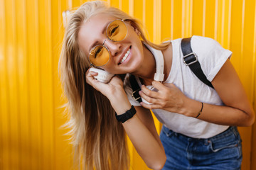 Fototapeta premium Wonderful girl in white t-shirt and jeans expressing positive emotions. Refined lady listening music in headphones on yellow background.