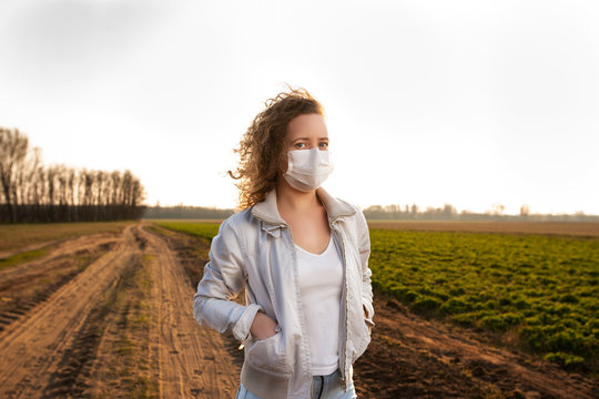 Beautiful casual woman walking on a path near meadow in the nature during covid-19 and wearing medical mask. Many people walking in the nature during quarantine and epidemic.