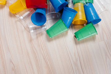 A large pile of multicolored plastic cups scattered on the floor with free space. Pollution of the environment by human waste