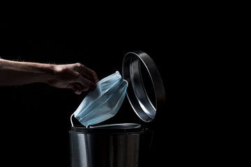 Hand, OP-Maske und Mülleimer, dunkler Hintergrund