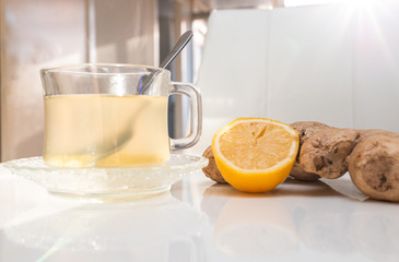 Glass cup of hot ginger tea with ginger rhizome (root) sliced and lemon, isolated on white background.