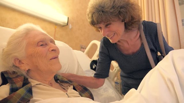 Happy 93 year old senior woman in hospital bed recovering, talking to her family. Slow motion, 4K UHD.