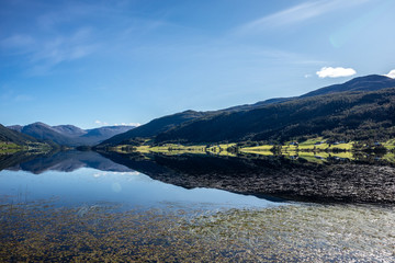 Norway mountains lake mirror on sunny day landscape. Hills reflection on water surface, blue sky, bright colors 