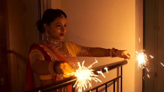 Young and beautiful Indian Bengali woman in Indian traditional dress is celebrating Diwali with fire crackers on a balcony in darkness. Indian lifestyle and Diwali celebration