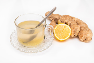Glass cup of hot ginger tea with ginger rhizome (root) sliced and lemon, isolated on white background.