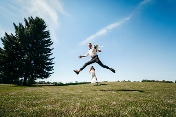 Young groom is jumping with happiness against the background of a young bride looking at him