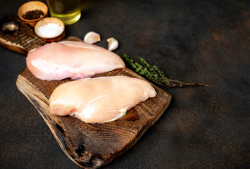 raw chicken breast on a cutting board with spices and a meat knife on a stone background 
with copy space for your text