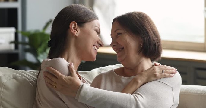Affectionate young woman cuddling bonding middle aged mature mother, enjoying sweete tender moment together at home. Head shot happy loving two female generations family communicating indoors.