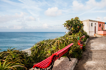 lonely red chair, on the edge of a cliff, on the stones and green of nature, facing the sea or the ocean