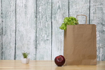 Recycled paper shopping bag with green salad and vegetables. Red apple and fruits.Eco product. Green plant on a white pot on a wooden background.