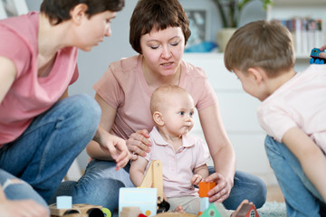 A young gay lesbian family with two children, a son and a daughter, spend time at home. They sit on the floor and play with children's toys.