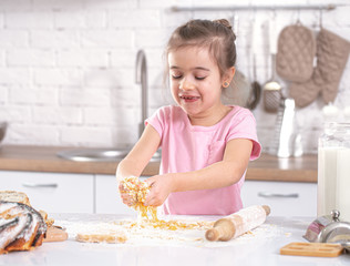 A cute little girl is cooking homemade cakes in the kitchen.