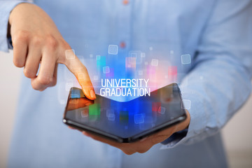 Young man holding a foldable smartphone with UNIVERSITY GRADUATION inscription, educational concept