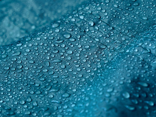 Rain water droplets on blue fiber waterproof fabric. Blue background.
