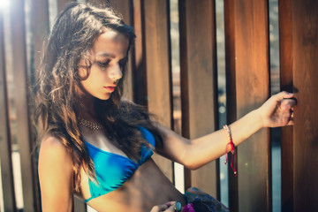 Portrait of a beautiful young girl in blue swimsuit leaned against a wooden fence. - obrazy, fototapety, plakaty