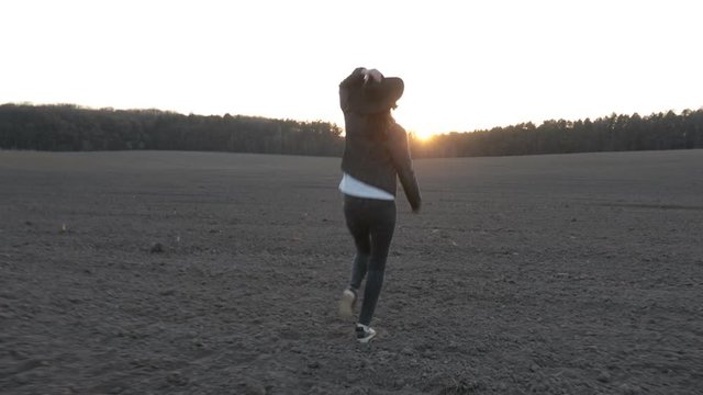 Cowgirl or cowboy girl walking on empty field at sunset wearing cawboy hat. 4K