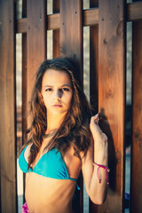 Portrait of a young girl in blue swimsuit leaned against a wooden fence. A svelte young black girl in a blue swimsuit is thoughtfully and sad looking in the camera while standing near a wooden fence