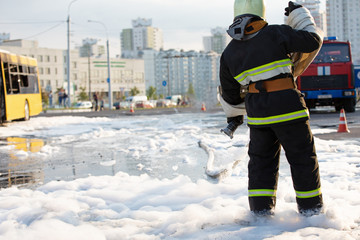 Fireman standing among firefighting foam and carrying fire hose reel after extinguish fire in public transit bus