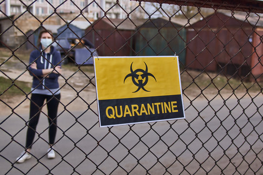 A girl is standing behind a fence with a yellow sign with the word Quarantine and a biohazard sign