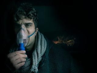 Dark Portrait of man using steam vapor inhaler nebulizer doing aerosol inhalation medicine...