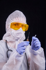 Protection against infection. The doctor is dressed in a protective suit, protective glasses and a protective mask holds a syringe with a vaccine in his hands. Isolated on a black background