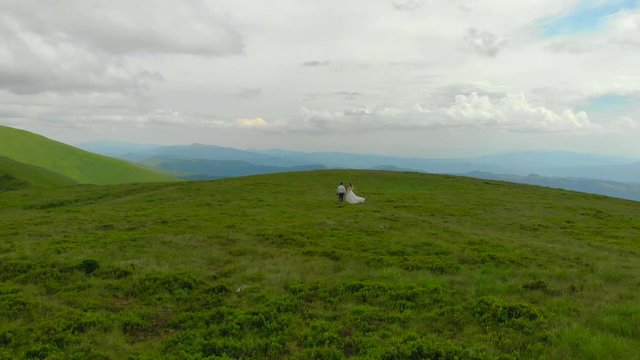 young wedding couple walking on top of green mountains. Against the backdrop of a mountain in love young people in wedding clothes. Aerial view. Mountain meadow and green grass
