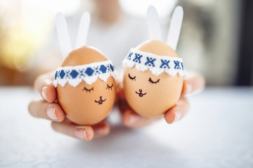 Two little easter eggs with a painted drawn rabbit faces and ears on them in the hands of a young boy teenager. Easter holidays decorations and preparations concept. Holy religious day.