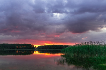 Fototapeta na wymiar bright sunset over a forest lake with voluminous clouds