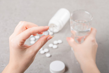The girl is holding a white tablet or vitamins or food Supplement in her hand, against the background of a table and a glass of water in her second hand. Concept of treatment, prevention or diet.