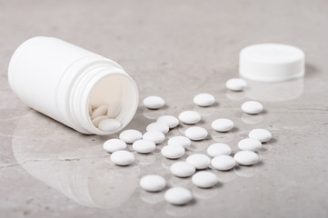 A white vial and a handful of white tablets or vitamins or nutritional supplements lying on a marble table.