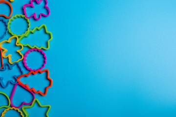 Multi-colored plastic forms of various shapes for the manufacture of cookies on a blue background. Frame for culinary concept. Flat lay with copyspace.