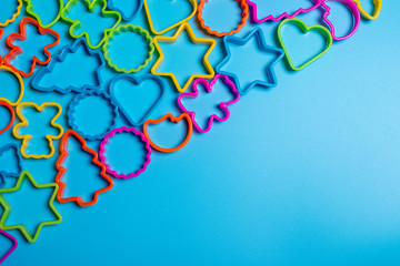 Multi-colored plastic forms of various shapes for the manufacture of cookies on a blue background. Frame for culinary concept. Flat lay with copyspace.