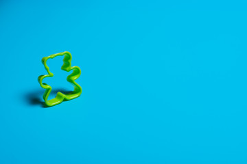 Green plastic cookie cutter for making cookies in the shape of a teddy bear on a blue background....
