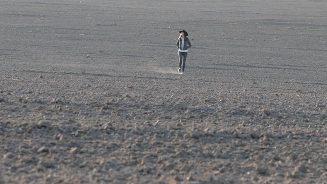 Cowgirl or cowboy girl walking on empty field at sunset wearing cawboy hat. 4K