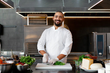 Handsome young African chef standing in professional kitchen in restaurant preparing a meal of meat...