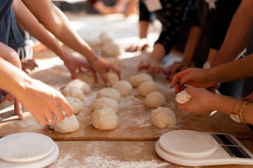 Close-up hands forming dough balls for baking buns on a wooden table during manufacture. Culinary...