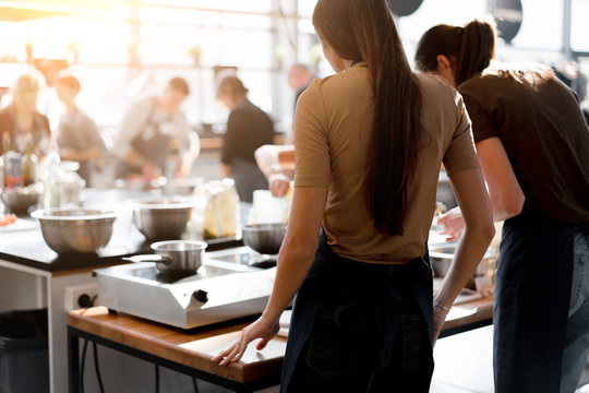 Culinary class. Back view of the process of cooking. Different unrecognizable people in gray apronsthe in the kitchen learn to cook