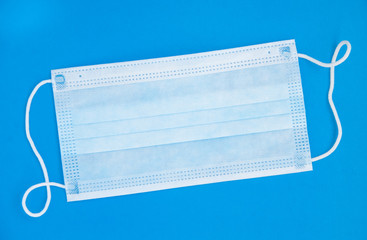 Medical surgical mask on a blue background. Surgical mask with rubber ear straps. Typical 3-ply surgical mask to cover the mouth and nose. Procedure mask from bacteria. Protection concept.