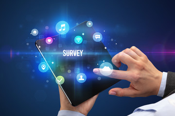 Businessman holding a foldable smartphone with SURVEY inscription, social media concept