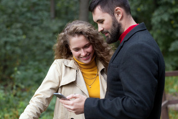 Obraz premium Young couple watch photos on smartphone in park