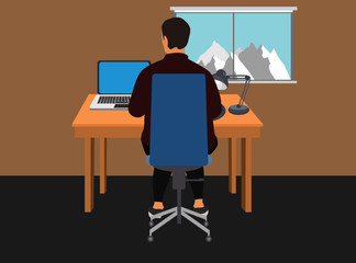 Man working at home. Sitting on a wheelchair working on a portable computer over a wooden table and next to a desk lamp. A window with mountains and a blue sky. Concept for working ar home.