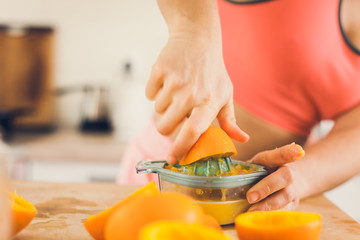 Young woman in sportswear squeezing oranges on a table, preparing juice.