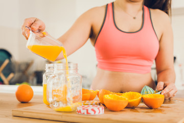 Young woman in sportswear pouring freshly squeezed orange juice in a jar.