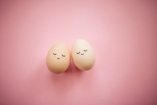 Two little easter eggs with a painted drawn happy faces on them in laying on the pink table isolated. Easter holidays decorations, preparations concept. Holy religious day. Copyspace, place for text.