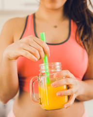 Young woman in sportswear holding a jar of freshly squeezed orange juice at home.