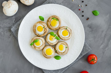 Stuffed mushrooms with quail eggs on a white plate with basil and thyme leaves on a dark concrete background. Easter appetizer. Horizontal orientation. Top view.