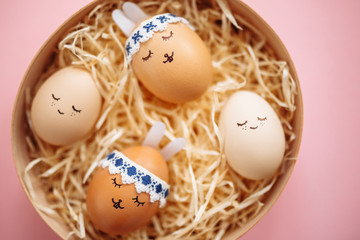Four little easter eggs with a painted drawn rabbit faces and ears laying in hay on the pink table isolated. Easter holidays decorations and preparations concept. Holy religious day. Copyspace.