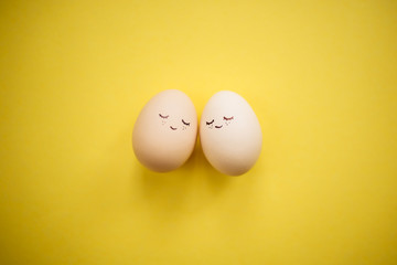 Two little easter eggs with a painted drawn happy faces on them laying on the yellow table isolated. Easter holidays decorations, preparations concept. Holy religious day. Copyspace, place for text.