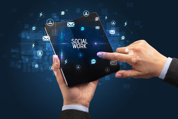 Businessman holding a foldable smartphone with SOCIAL WORK inscription, social networking concept